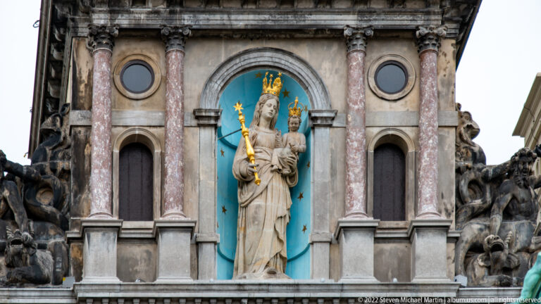 Crowned Madonna and Child holding a gilded scepter in a turquoise niche framed by columns and dark sculptural ornament.