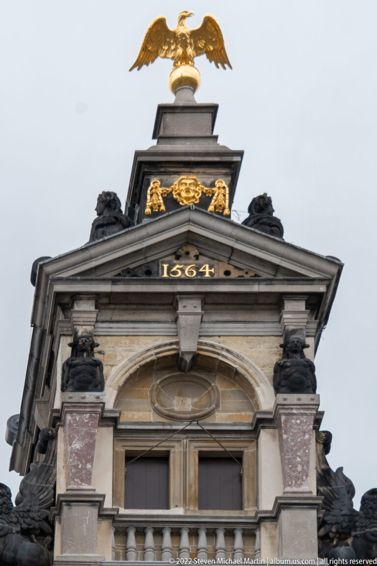 Historic gable dated 1564, topped by a gilded eagle and enriched with dark sculpture, gold ornament, and marble-like columns.