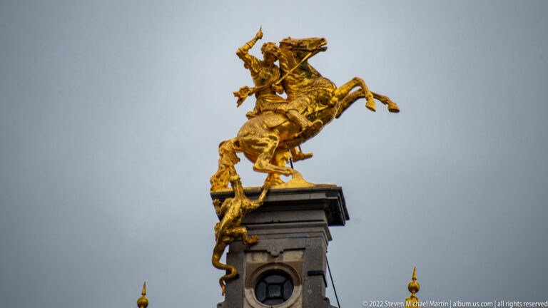 Gilded Saint George on a rearing horse above a dragon, mounted high on an Antwerp rooftop pedestal.