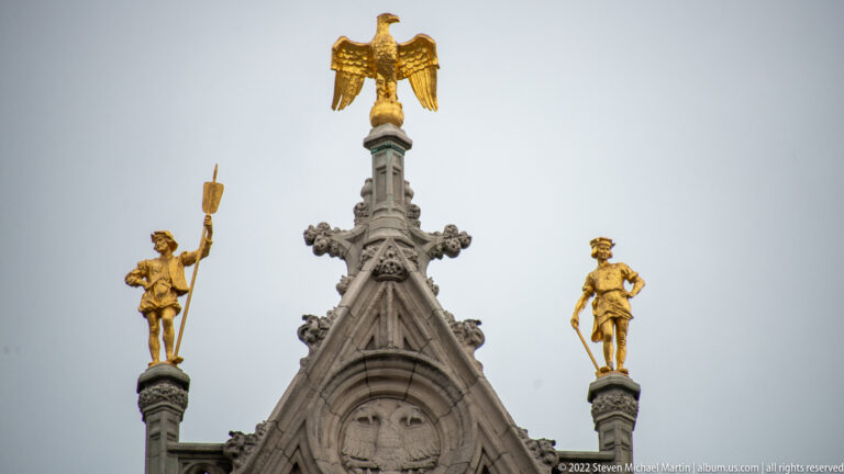 Gothic stone gable crowned by a gilded eagle and flanked by two gilded standing figures on pinnacles.