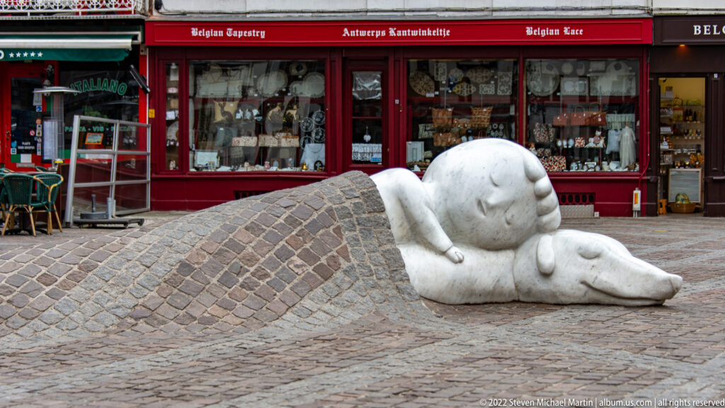Sleeping boy and dog of the Nello and Patrasche monument emerging from beneath a blanket of raised cobblestones.