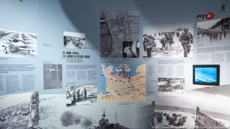 Museum wall labeled 6 Juin 1944 with wartime photographs, maps, text panels, and a small video screen.