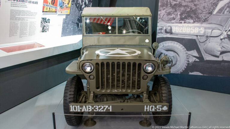 Front view of an olive-drab U.S. military jeep with white star, round headlights, slotted grille, windshield, and bumper markings.