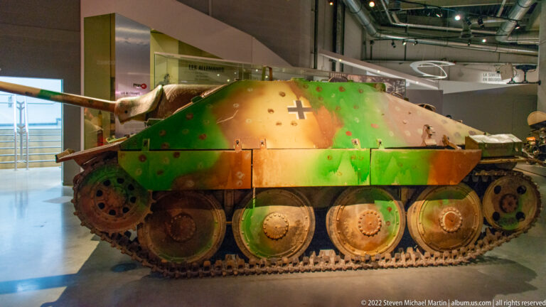 Side view of a camouflaged German Jagdpanzer 38(t) Hetzer with sloped casemate, fixed gun, tracks, and German cross.