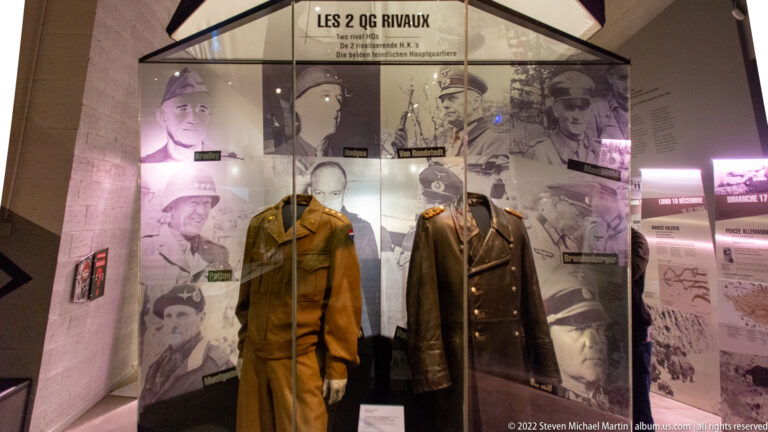 Two German uniformed mannequins in a glass case beneath the title Les 2 QG Rivaux and a wall of officer portraits.