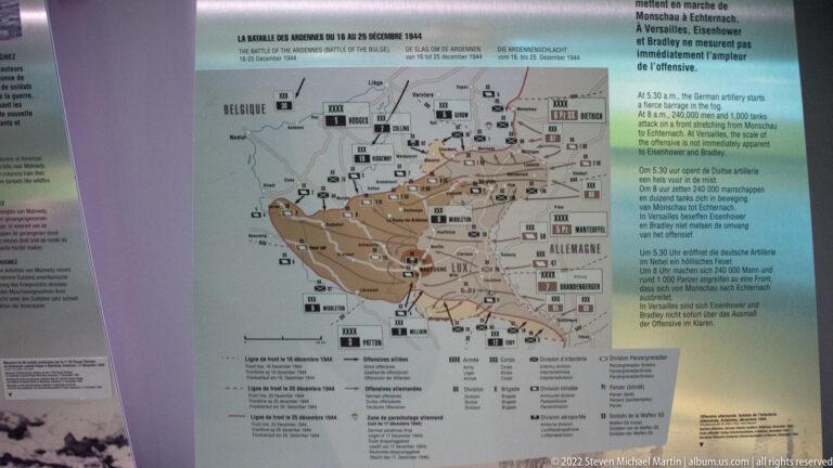 Operational map of the Ardennes with unit symbols, arrows, front lines, and a brown-shaded battle area across Belgium and Luxembourg.