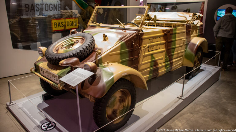 Camouflaged German Volkswagen Kübelwagen with open cabin, rear spare tire, exposed fenders, and simple military bodywork.