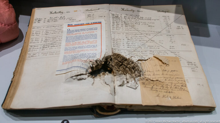 Open handwritten ledger with loose forms, notes, and a small fabric or fur fragment laid across the pages.