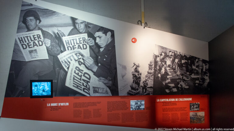 Museum wall with newspapers announcing Hitler's death beside a panel on Germany's capitulation.