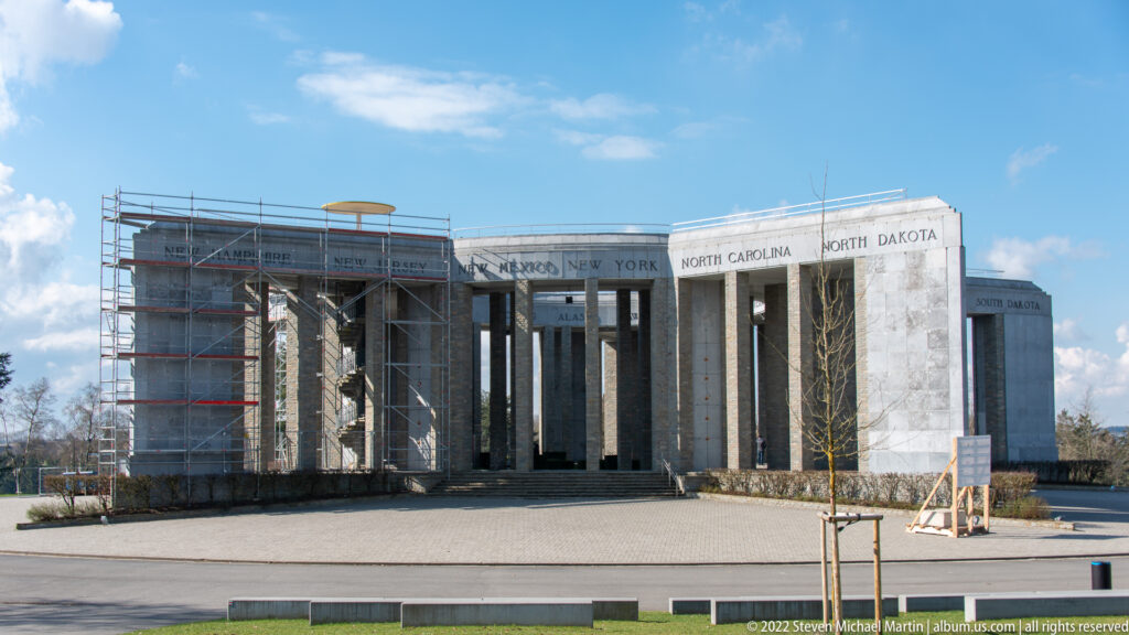 Wide exterior view of the Mardasson Memorial with scaffolding on the left side and state names above the columns.