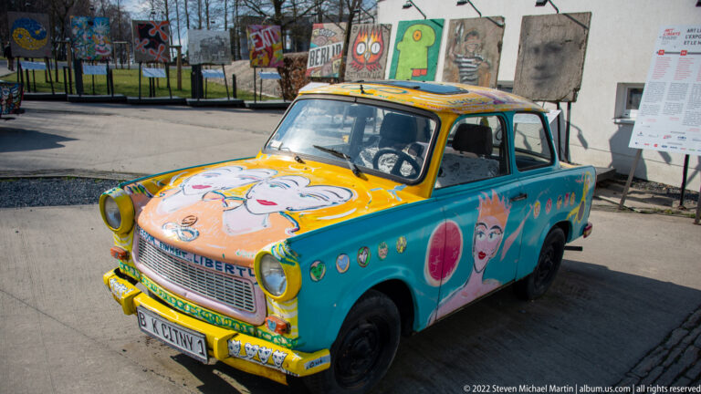 Turquoise-and-yellow compact sedan painted with portraits, symbols, and text, displayed outdoors.