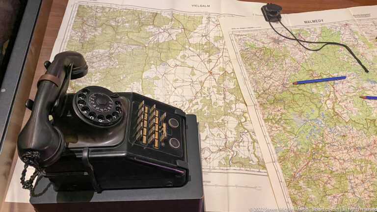Black rotary field telephone placed on top of detailed military maps with colored markings.