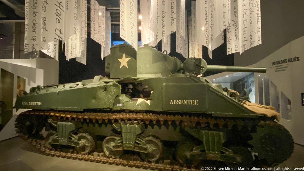 Olive-drab American tank with white star, long gun barrel, and 'ABSENTEE' painted on its side.