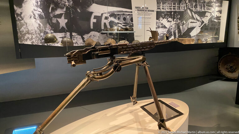 Heavy machine gun mounted on a three-legged tripod in the museum gallery.