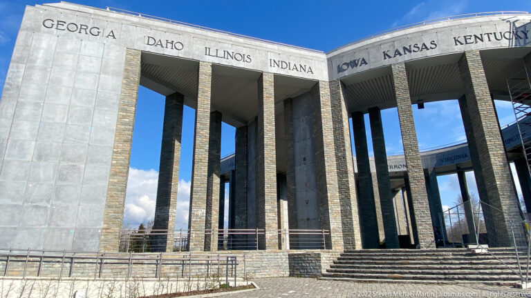 Exterior corner of the Mardasson Memorial with steps, tall stone piers, and several U.S. state names carved above.