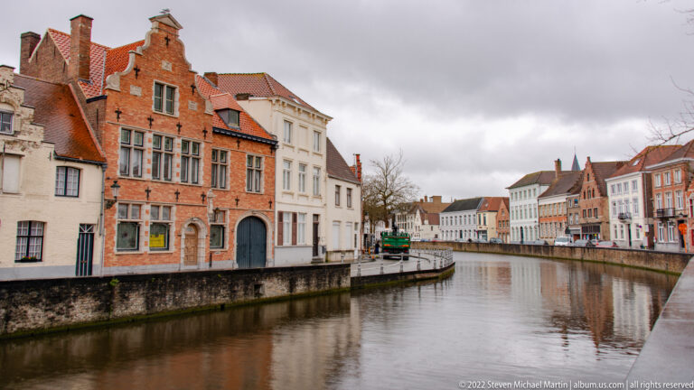 Narrow canal curves between historic brick and stucco houses with red tile roofs in Bruges.