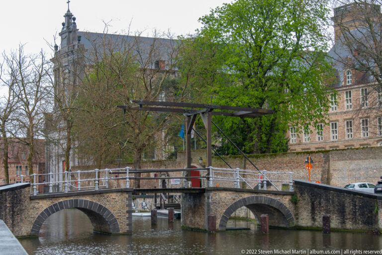 Low stone bridge with multiple arches and a timber lifting structure over a Bruges canal.