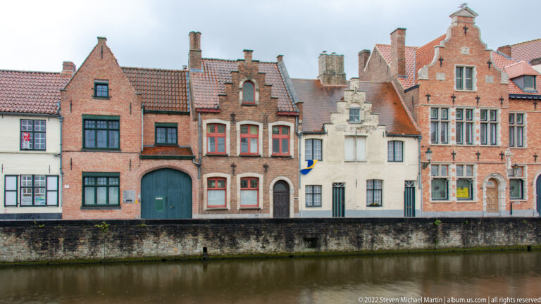 Closely packed historic houses with varied stepped and sculpted gables face a Bruges canal.