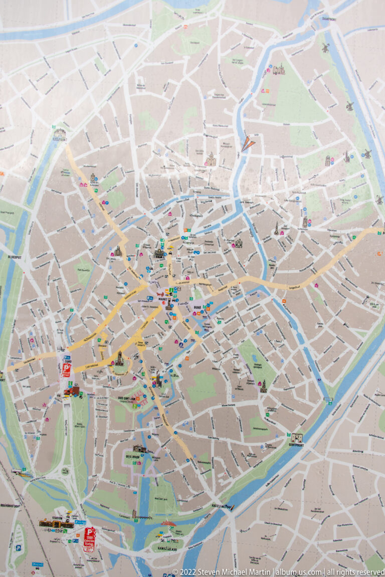 Printed visitor map of Bruges showing the historic street grid, surrounding canals, and colored site markers.