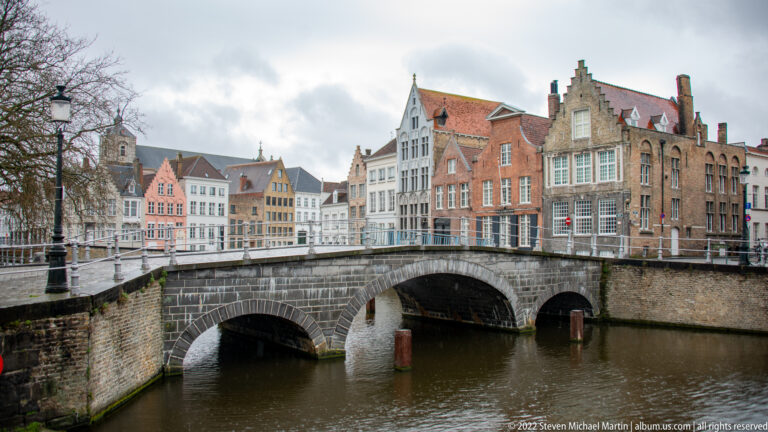 Large arched stone bridge over a canal with ornate historic gabled buildings immediately behind in Bruges.