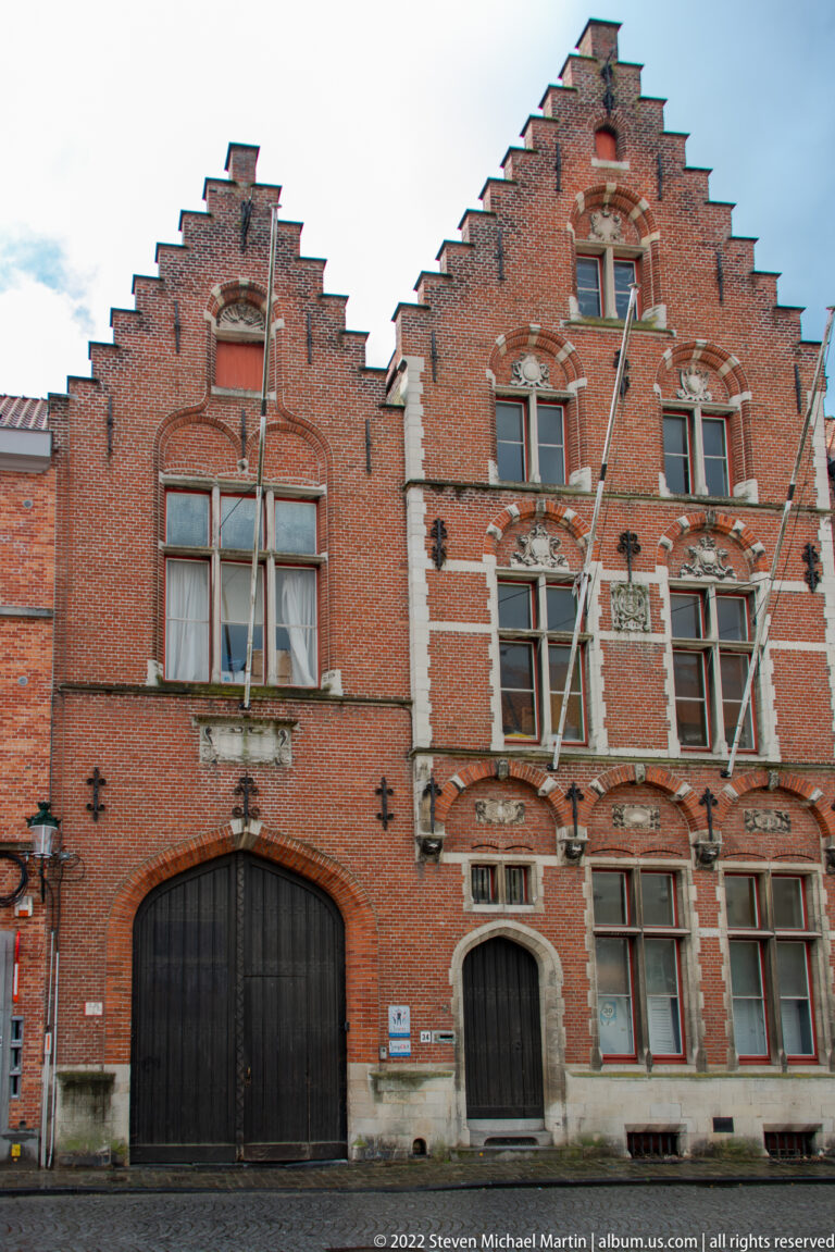 Two red-brick stepped-gable façades with black doors, stone-framed windows, and decorative masonry in Bruges.