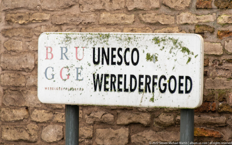 Weathered sign reading Brugge and UNESCO Werelderfgoed mounted against an old brick wall.