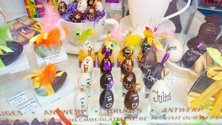 Colorful chocolate figures, eggs, ribbons, and handwritten labels arranged in a Bruges confectionery window.
