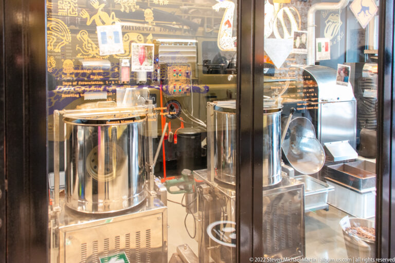 Stainless-steel vats and chocolate-making machinery seen through reflective glass in a Bruges confectionery.