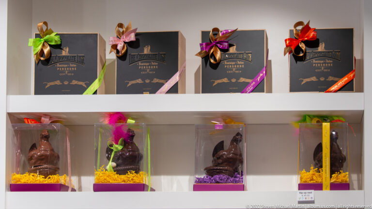 Dark chocolate gift boxes with colorful ribbons above molded chocolate figures in clear display cases.