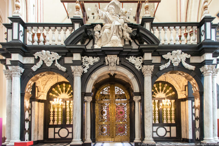 Black-and-white marble church portal with gilded central door, columns, garlands, and sculpted figures inside Saint-Salvator Cathedral.