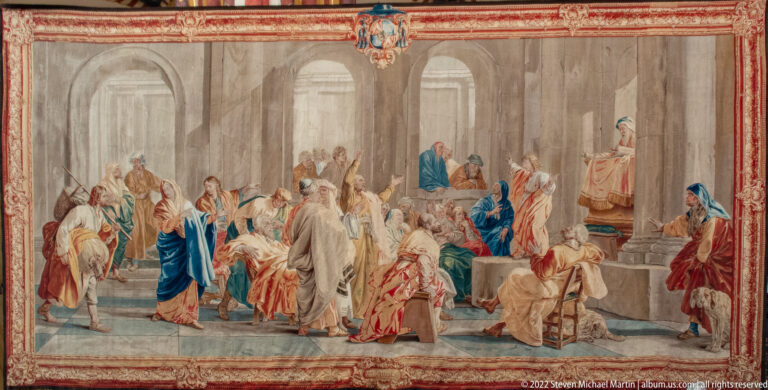 Large woven religious tapestry with many robed figures gathered in a classical architectural interior.