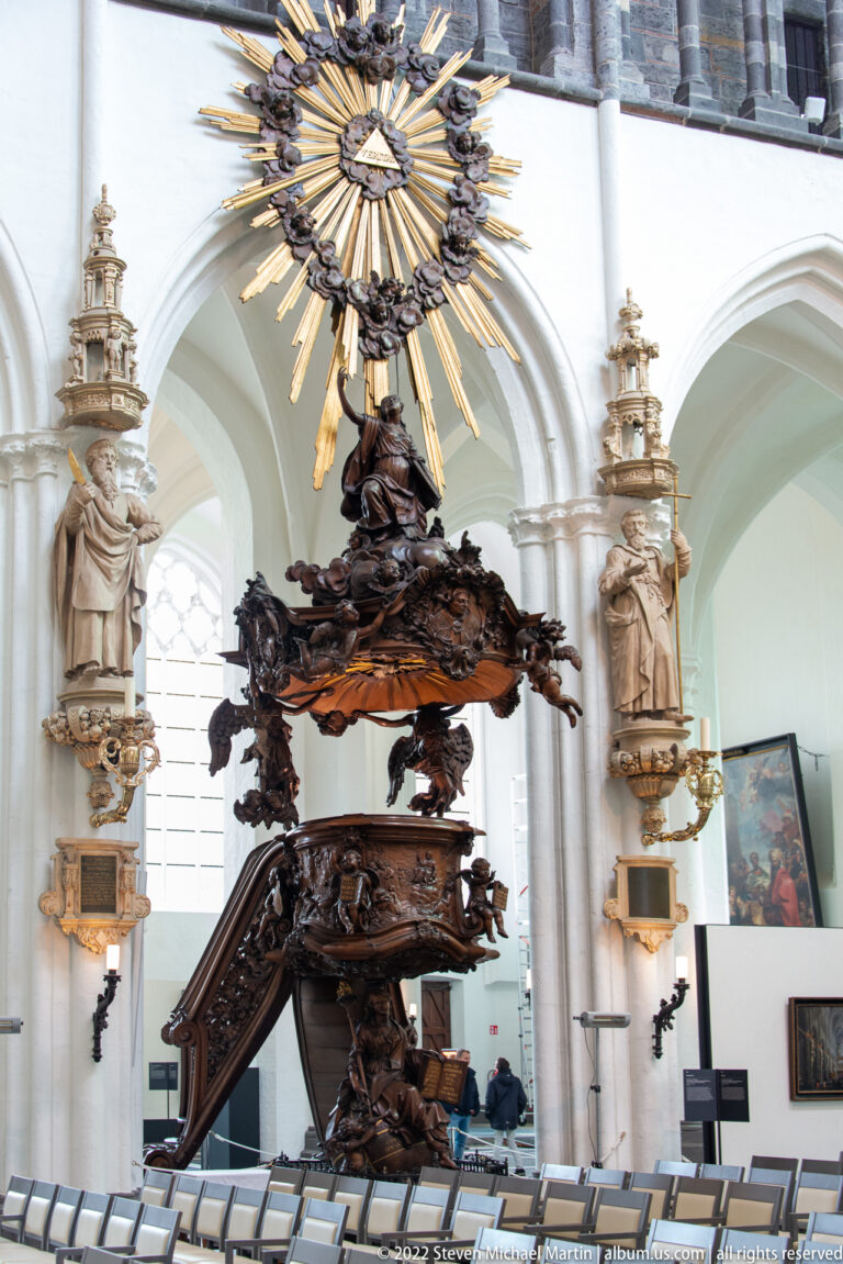 Dark carved wooden pulpit with sweeping stair, sculpted figures, and radiant canopy inside the Church of Our Lady.