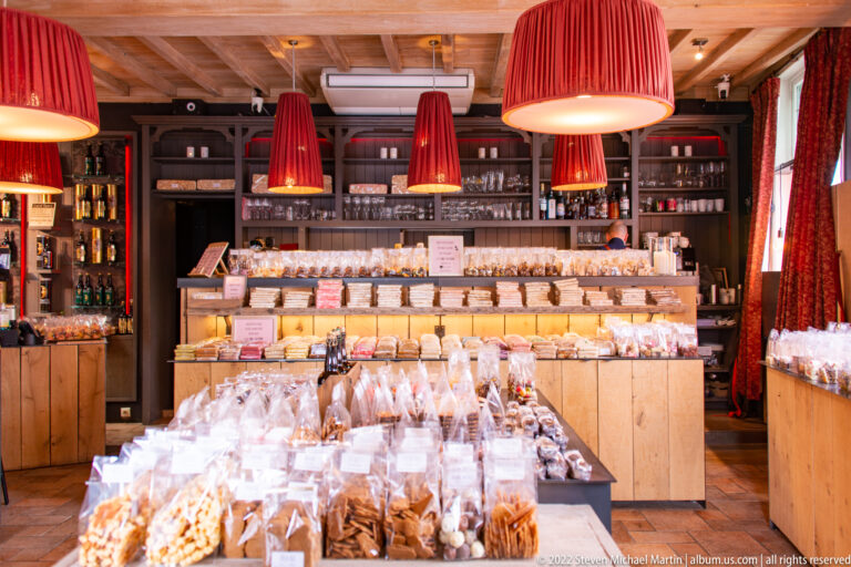 Bruges sweets shop with wooden displays of packaged confections beneath large red pendant lamps.