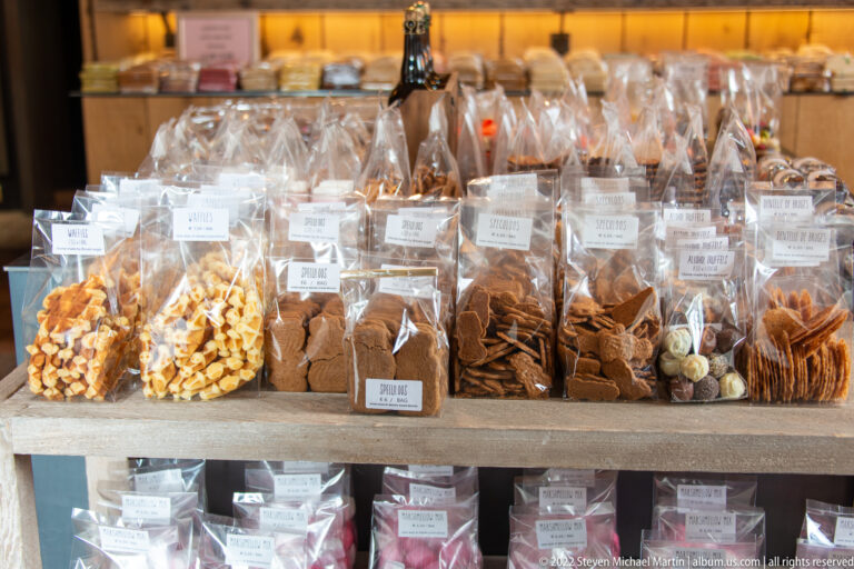 Clear bags of assorted biscuits and cookies arranged in rows on a wooden display table in Bruges.