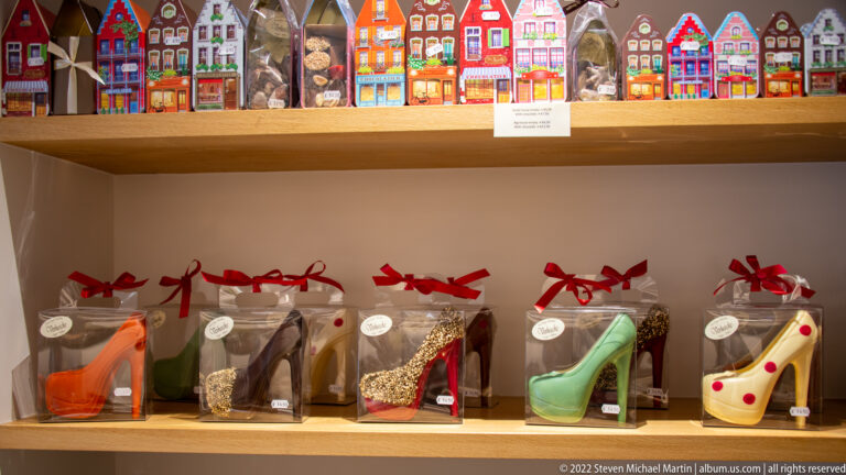 High-heeled shoe chocolates in clear ribbon-tied boxes, with colorful miniature house packages on the shelf above.