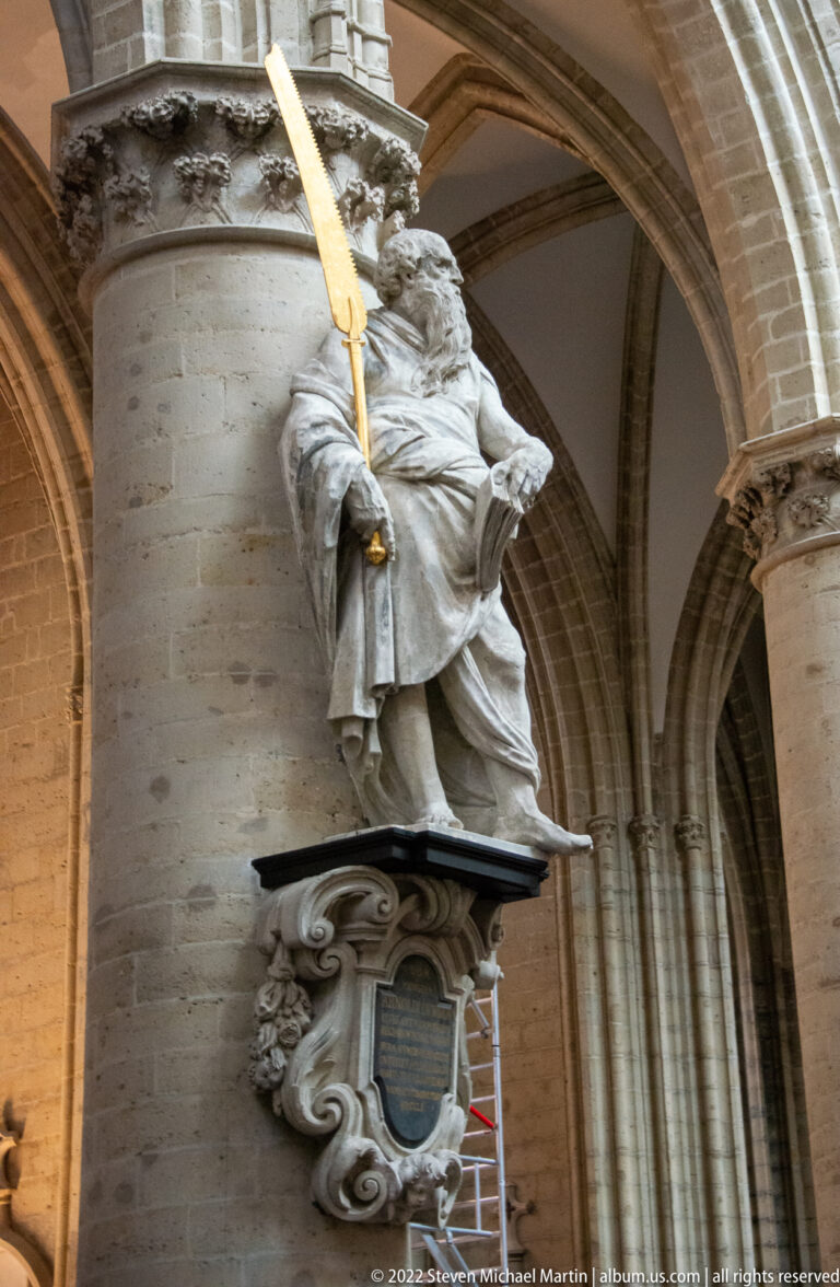 Life-size stone apostle figure on an ornate bracket, holding a gilded attribute beneath the cathedral’s ribbed vaults.