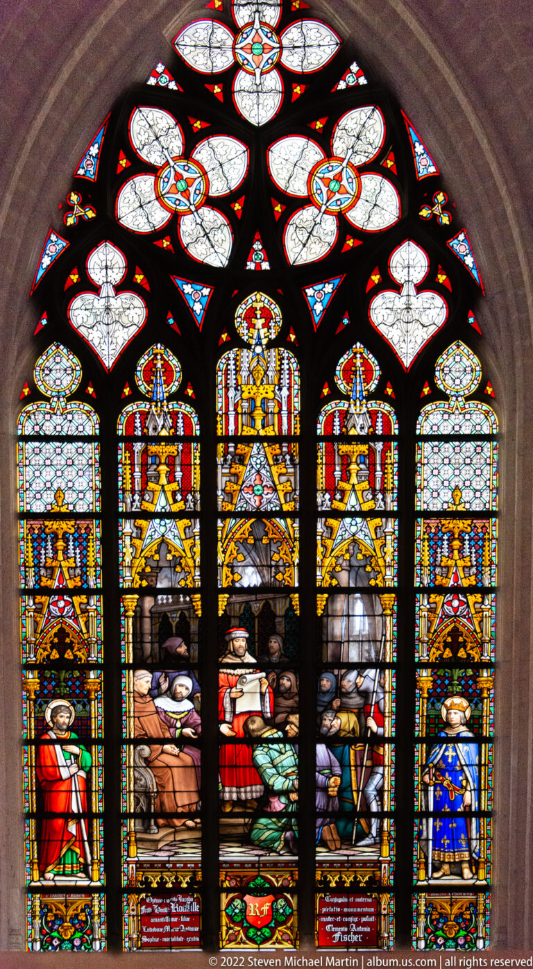 Arched stained-glass window with a dark central seated figure, colorful attendants, heraldic panels, and patterned tracery.