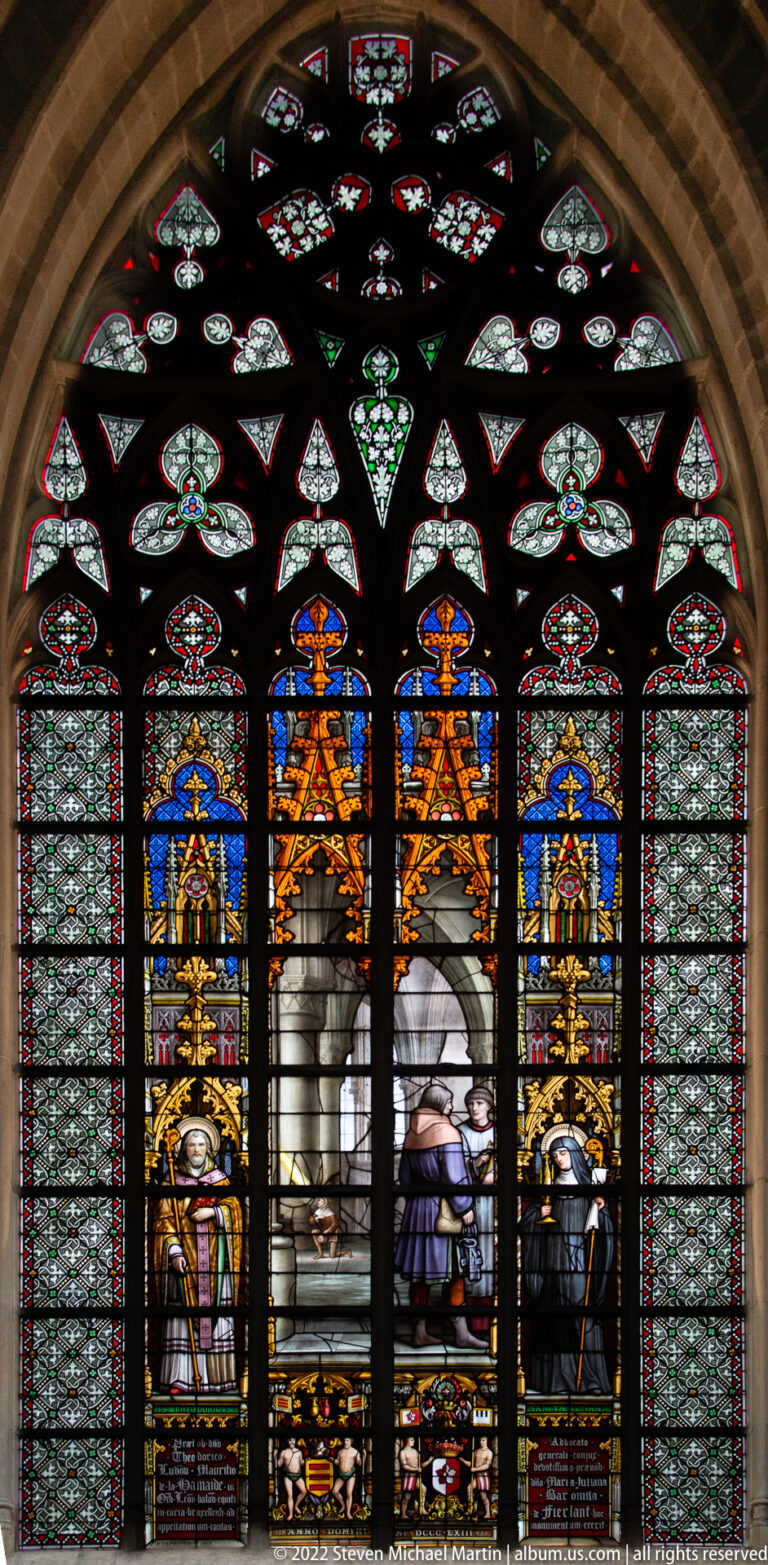 Large arched stained-glass window with robed clerics in side lancets and a central narrative scene beneath ornate tracery.
