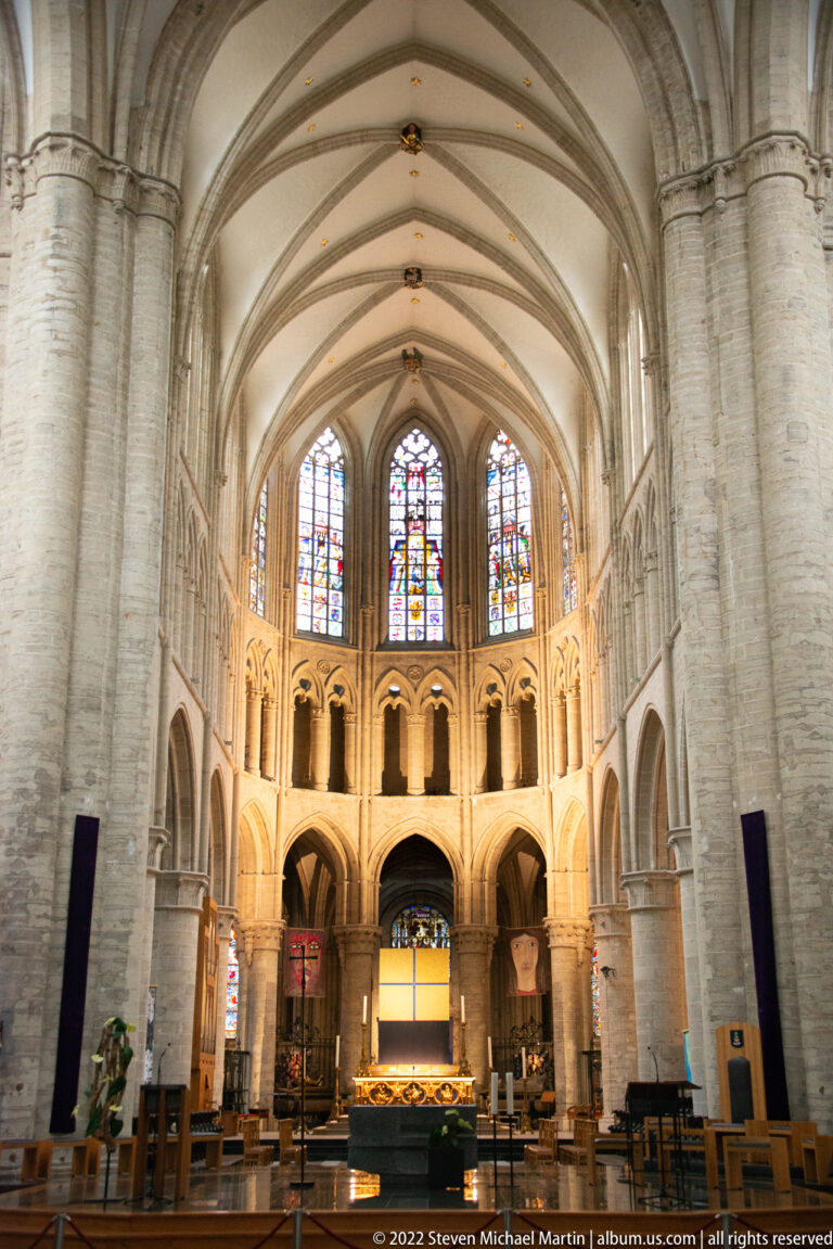 Wide symmetrical view of the cathedral’s eastern interior with ribbed vaults, side arcades, stained glass, and illuminated sanctuary.