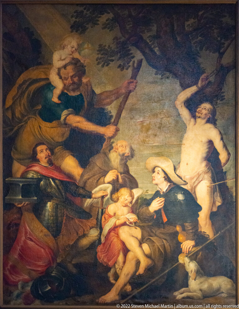 Large religious painting with clustered figures surrounding an infant at the center, framed by dark robes and warm-toned drapery.