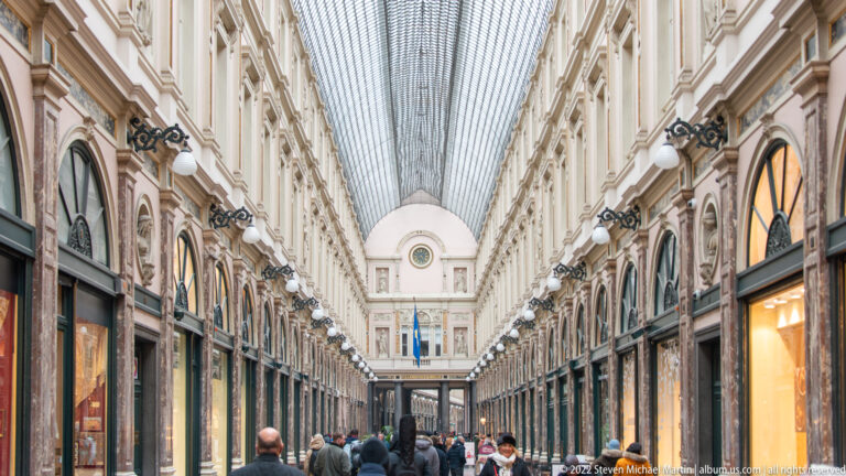 Long interior view of the Galeries Royales Saint-Hubert beneath a glass barrel roof, with arched shops and pedestrians.