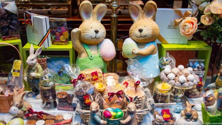Easter confectionery window with two large rabbit figures, wrapped chocolates, foil eggs, truffles, and gift baskets.