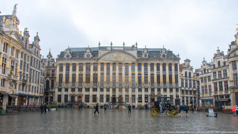 Wide Grand-Place view centered on the Maison des Ducs de Brabant, flanked by ornate guildhouses under an overcast sky.