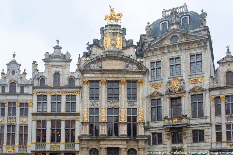 Upper façades of ornate Grand-Place guildhouses with curving gables, columns, gilded ornament, and a mounted figure on one roof.