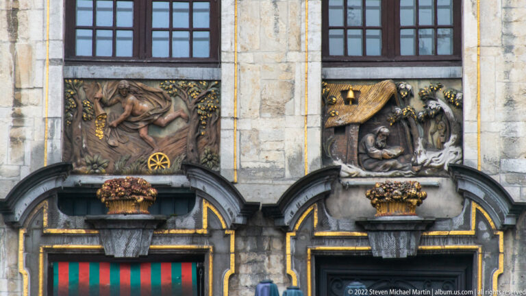 Two narrative relief panels above arched doorways, with sculpted figures, a wheel motif, and scattered gilded details.