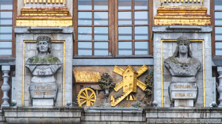 Two inscribed stone busts labeled Carolus Dux Burg and Maximilianus Roman Rex flank a central windmill-and-cart relief.