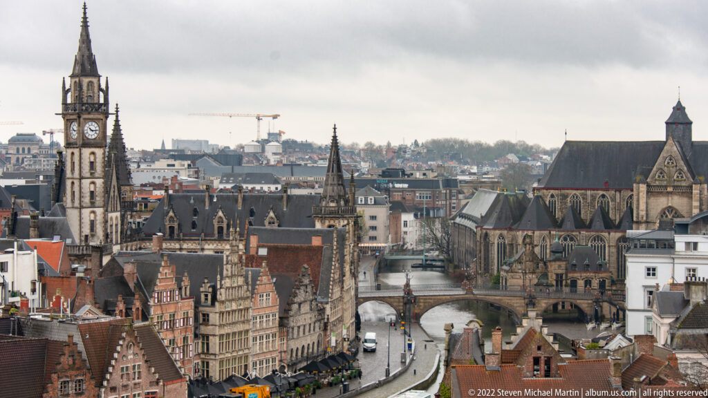 Elevated Ghent city view with a clock tower, Gothic church, gabled houses, streets, and a canal crossing.