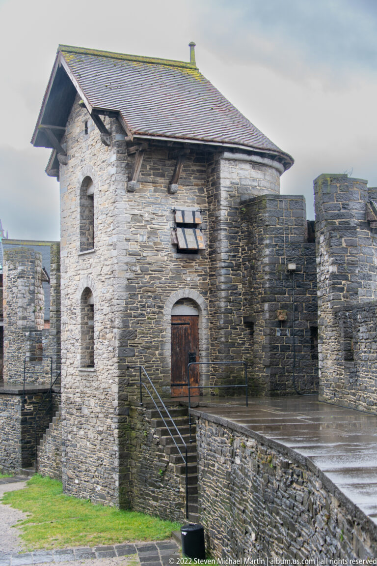 Roofed stone gate tower with arched doorway, narrow windows, crenellated walls, and a raised approach inside Gravensteen.