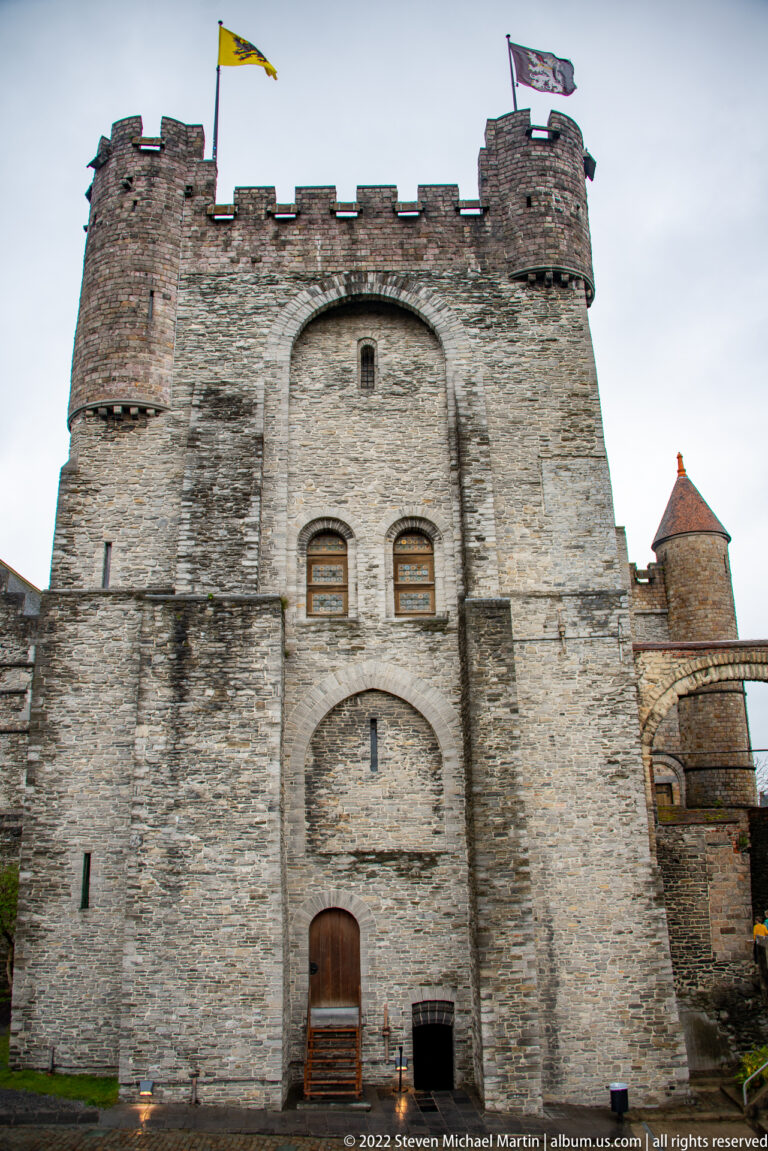 Massive stone keep at Gravensteen with crenellations, narrow arched openings, and flags above the roofline.