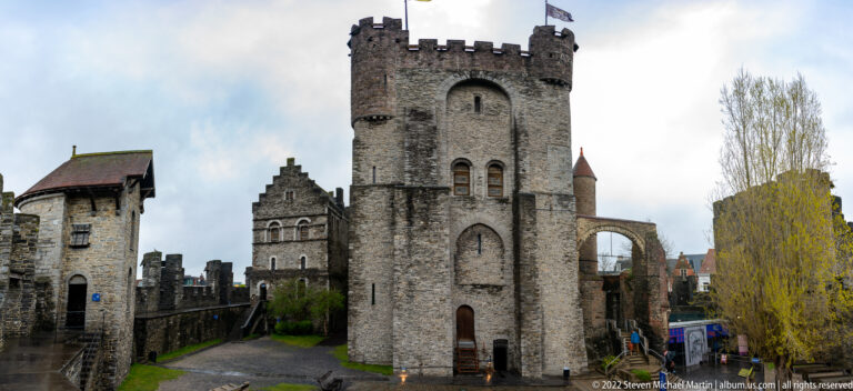 Tall crenellated stone tower in Gravensteen's inner court with lower towers, walls, and gabled buildings around it.